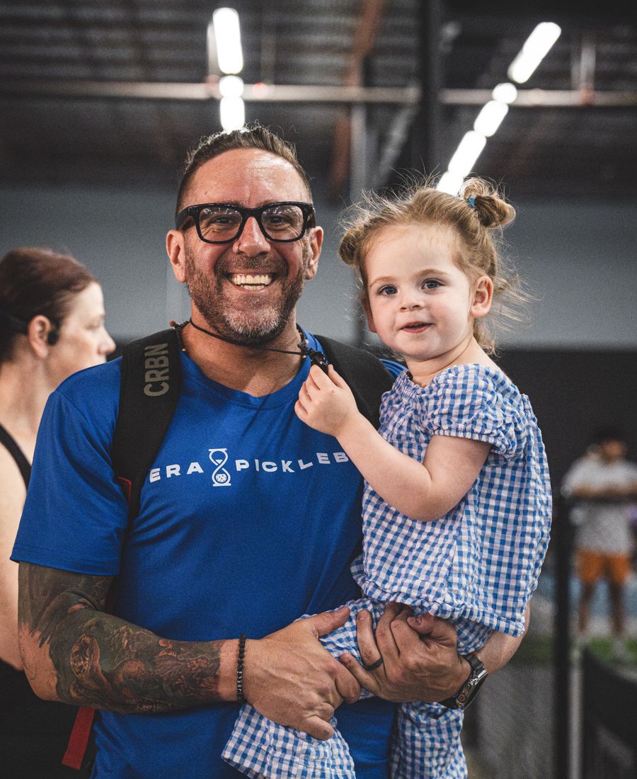 Mike "Batman" Cohen at a pickleball tournament, holding his daughter